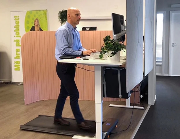 En man i kostym går på ett gåband medan han arbetar vid datorn vid sitt skrivbord på kontoret.