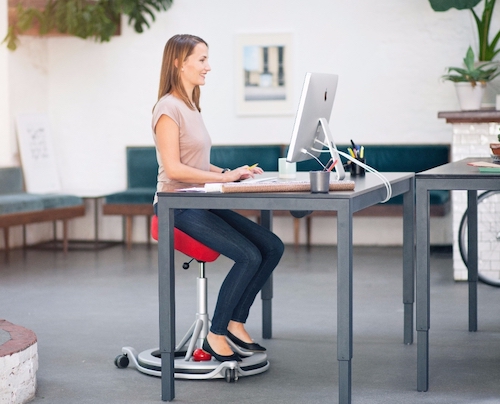 En kvinna sitter i en röd ergonomiskt korrekt kontorsstol framför sitt skrivbord och arbetar på sin dator.